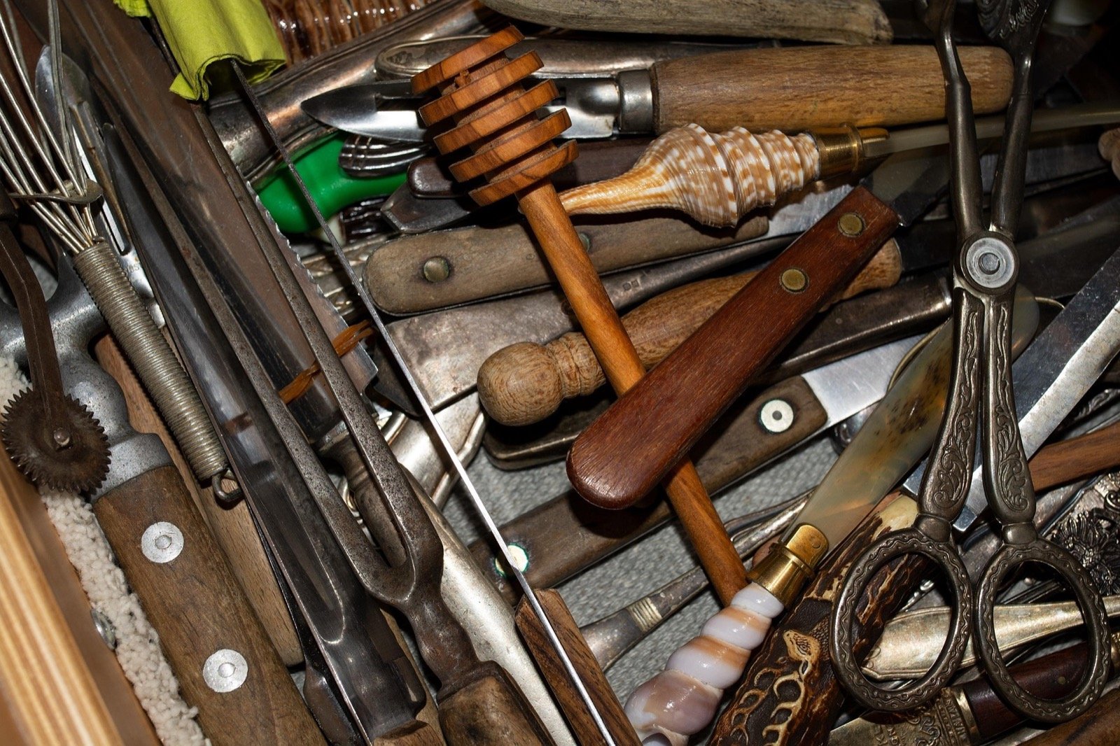 A crowded drawer filled with mixed household items and utensils.
